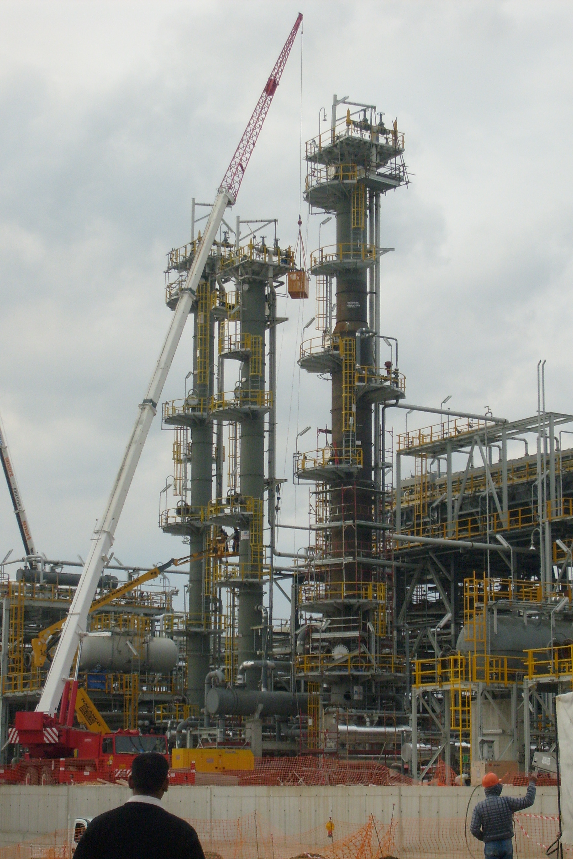 Impianto industriale con colonne verticali, tubazioni, passerelle e gru di cantiere